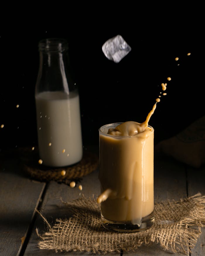 Captivating black background image of milk tea splash showcasing ice cube motion and milk in the background.